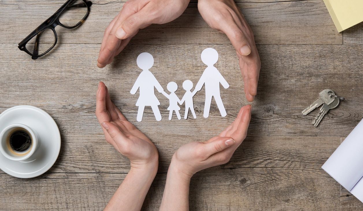 Hands protecting a paper family cutout — symbolizing family protection